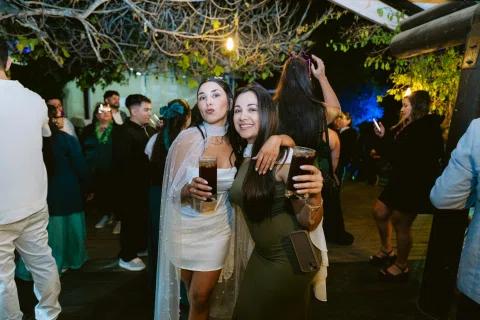 Dos mujeres posan juntas con bebidas en la mano bajo luces nocturnas.