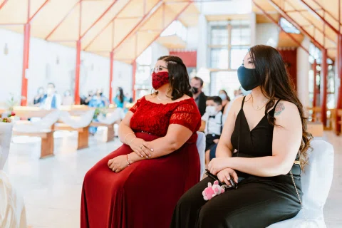 Dos mujeres con mascarillas, una con vestido rojo y otra con vestido negro, permanecen sentadas durante la ceremonia.