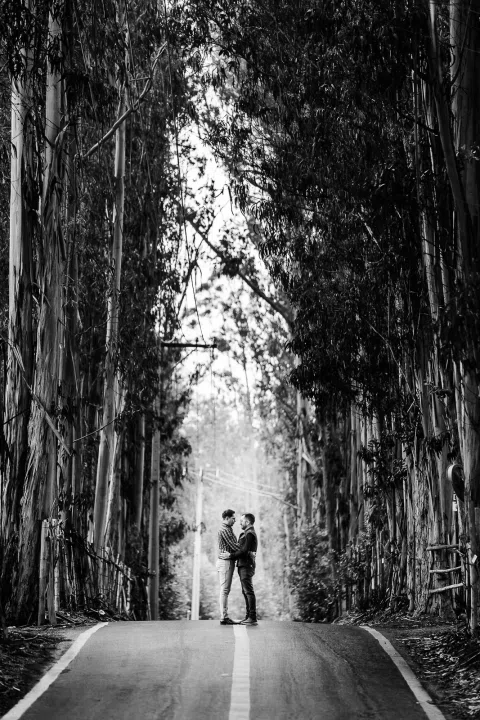 Dos personas de pie frente a frente en una carretera entre árboles, en una fotografía en blanco y negro.