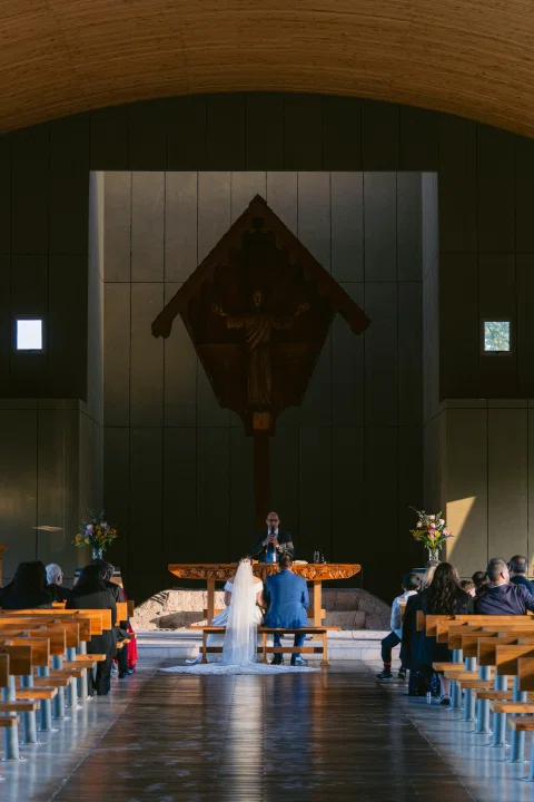 Dos personas están sentadas a distancia frente al altar en el interior de una capilla.
