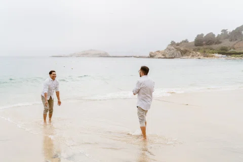 Dos personas frente a frente en la orilla de la playa, con agua poco profunda alrededor de los pies.