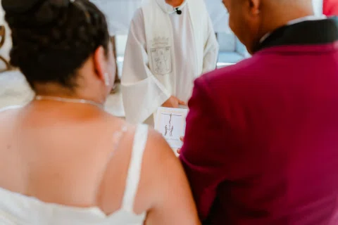 Mujer con vestido blanco y hombre con traje burdeos vistos de espaldas frente a una persona con vestimenta blanca.