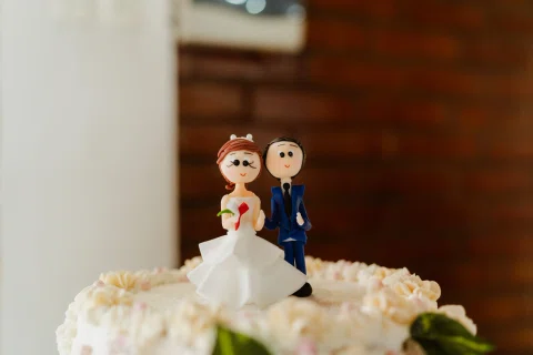 Dos figuras decorativas, una con vestido blanco y otra con traje azul, están sobre una torta blanca.
