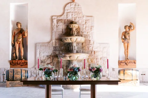 Fuente de piedra y mesa decorada con flores dentro de un salón.