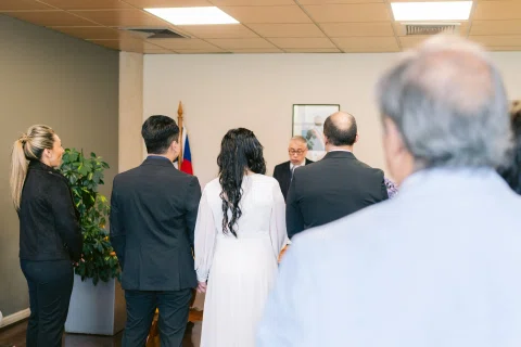 Grupo de personas visto de espaldas permanece frente a una mesa dentro de una sala.
