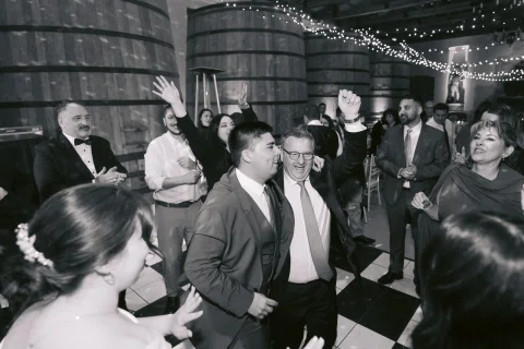 Grupo de hombres baila y levanta los brazos en una fotografía en blanco y negro.