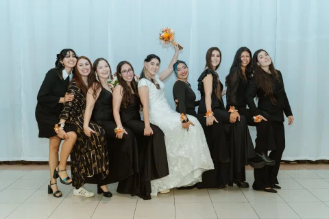 Grupo de mujeres posa junto a una mujer con vestido blanco que levanta un ramo de flores.