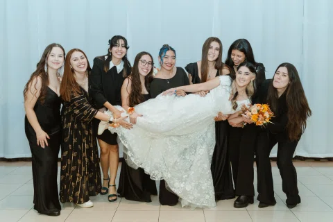 Grupo de mujeres sostiene horizontalmente a una mujer con vestido blanco mientras posan juntas.