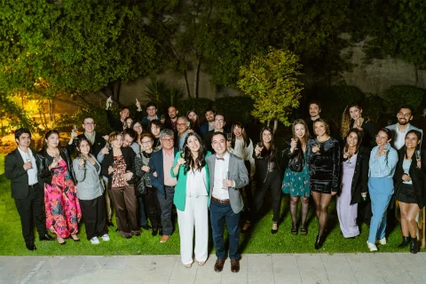 Grupo numeroso de personas posa al aire libre de noche.