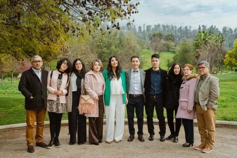 Grupo numeroso de personas posa al aire libre junto a un parque.