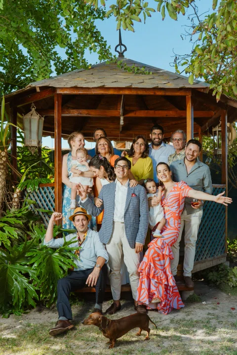 Grupo numeroso de personas posa frente a un gazebo de madera en el jardín.