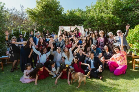Grupo numeroso de personas posa en el jardín con varios brazos levantados.