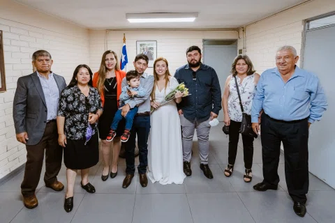Grupo de personas, incluida una mujer con vestido blanco y un niño, posando dentro de una sala.