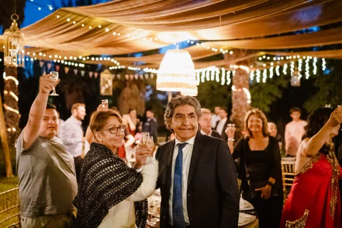 Varias personas levantan copas durante un brindis en la recepción, con un hombre de traje oscuro en primer plano.