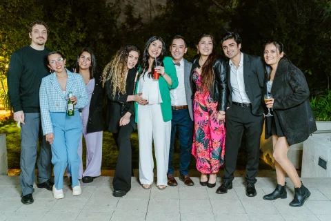 Grupo de personas posa al aire libre de noche; varias sostienen copas y botellas.