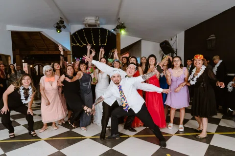 Grupo de personas posa sobre la pista de baile usando accesorios de fiesta y levantando los brazos.