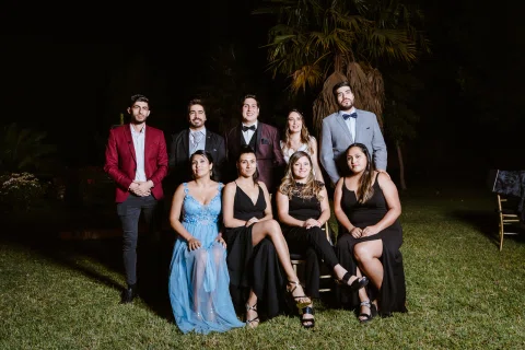 Grupo de personas posa junto en el exterior durante la noche, algunas de pie y otras sentadas.