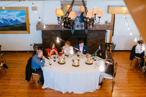 Grupo de personas sentado alrededor de una mesa frente a una gran chimenea.