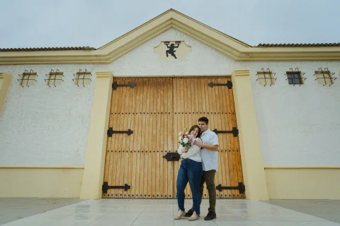 Hombre abraza a una mujer frente a un gran portón de madera.