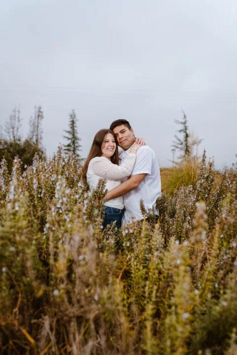 Hombre abraza a una mujer en medio de vegetación y flores.
