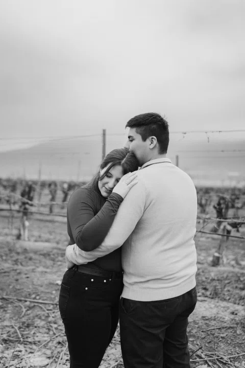 Hombre abraza a una mujer entre viñas en un retrato vertical en blanco y negro.