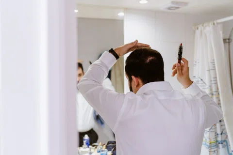 Hombre ajustando su cabello frente a un espejo antes de la ceremonia.