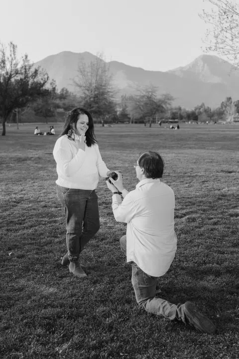 Hombre arrodillado frente a una mujer en el césped, fotografiados en blanco y negro.