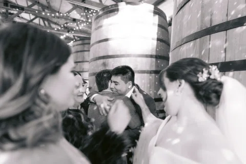 Hombre besa la mejilla de una mujer mientras otras personas aparecen alrededor, en blanco y negro.