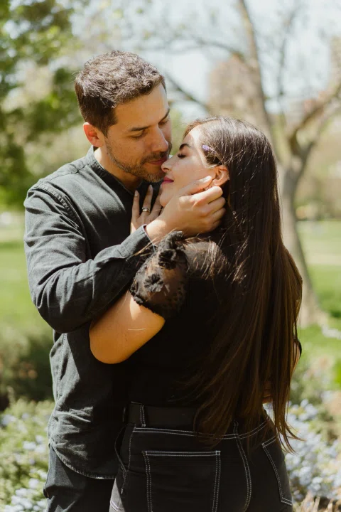 Hombre besando el rostro de la mujer mientras ella cierra los ojos en el parque.