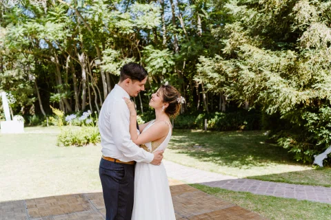 Hombre con camisa blanca y mujer con vestido blanco se besan en un jardín.