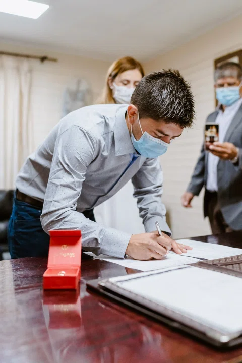 Hombre con camisa celeste inclinado sobre una mesa mientras firma un documento.