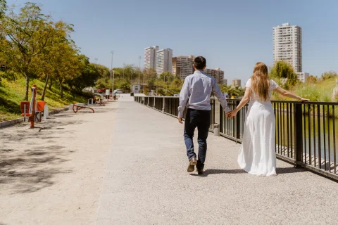 Hombre con camisa celeste y mujer con vestido blanco caminan de espaldas por un sendero de un parque.