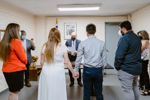 Hombre con camisa celeste y mujer con vestido blanco vistos de espaldas, con varias personas alrededor.
