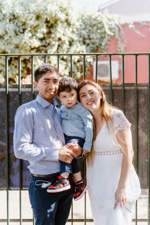 Hombre con camisa celeste sostiene a un niño junto a una mujer con vestido blanco.