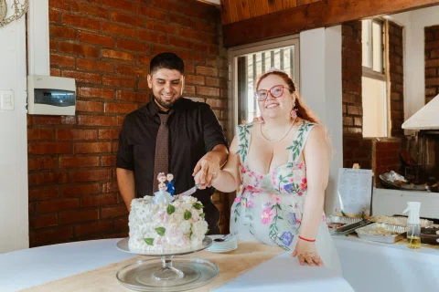Hombre con camisa negra y mujer de cabello rojo cortan juntos una torta sobre una mesa.