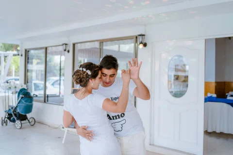 Hombre con camiseta gris y mujer con camiseta blanca bailan juntos en un espacio interior.