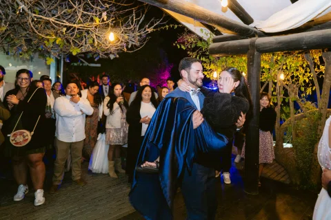 Hombre con capa azul baila con una mujer mientras varias personas observan al fondo.