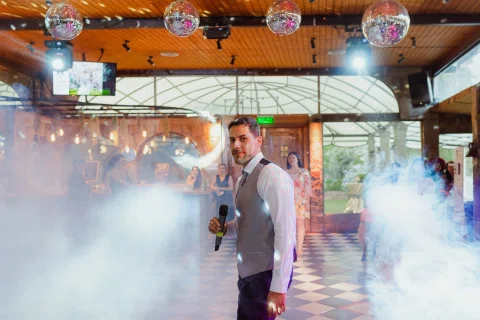 Hombre con chaleco sostiene un micrófono en la pista rodeado de humo escénico y luces.