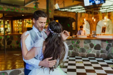 Hombre con chaleco y mujer con vestido blanco bailan abrazados en la pista bajo luces verdes.