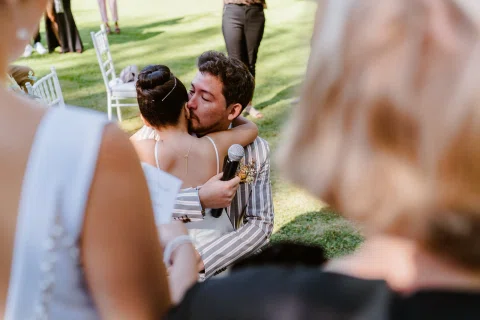 Hombre con chaqueta a rayas abraza a una niña con vestido blanco en un jardín.