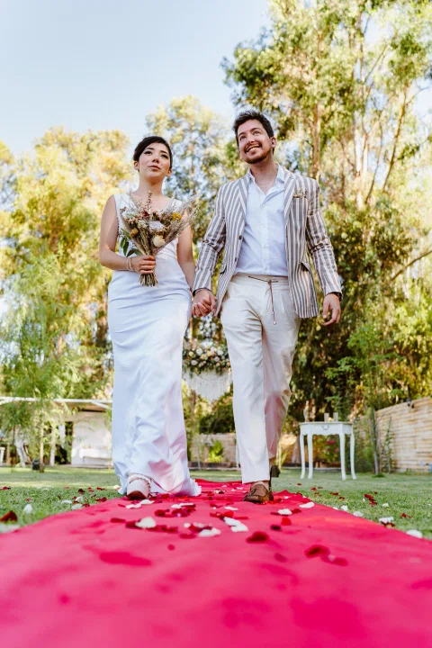 Hombre con chaqueta a rayas y mujer con vestido blanco están de pie juntos sobre una alfombra roja.