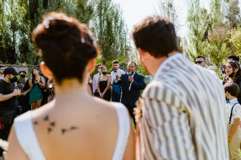 Hombre con chaqueta a rayas y mujer con vestido blanco vistos de espaldas frente a un grupo de personas.