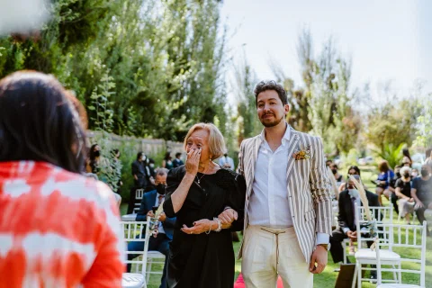 Hombre con chaqueta a rayas sonríe junto a una mujer con vestido negro en un jardín.