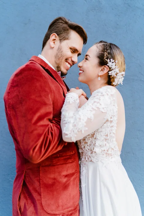 Hombre con chaqueta roja y mujer con vestido blanco sonríen frente a frente en un retrato cercano.