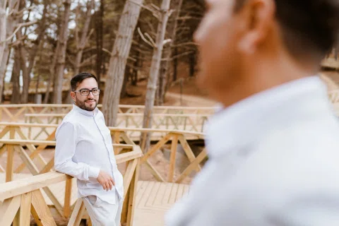 Hombre con lentes mira hacia otra persona desenfocada sobre un puente de madera.