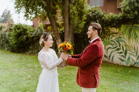 Hombre con chaqueta roja entregando un ramo de girasoles y flores naranjas a una mujer.