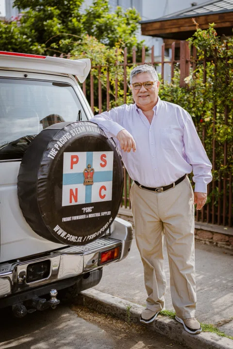 Hombre de pie junto a la parte trasera de un vehículo estacionado.
