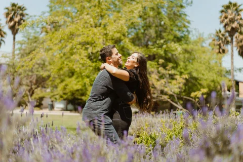 Hombre levantando a la mujer entre flores lilas en el parque.