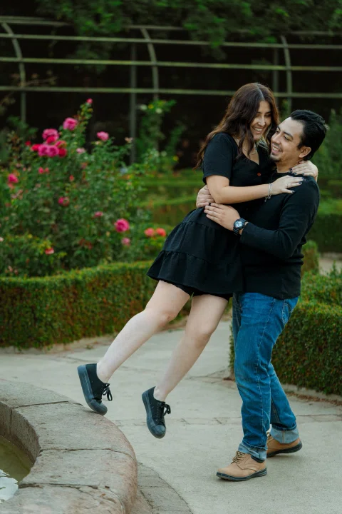 Hombre levantando a la mujer en brazos junto a un rosal.