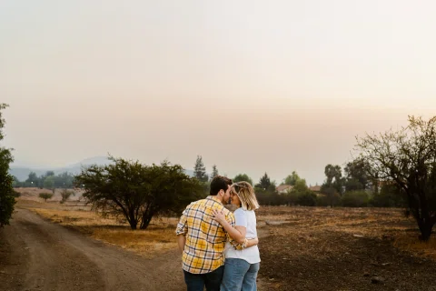 Hombre y mujer se abrazan en un camino rural bajo luz suave de atardecer.